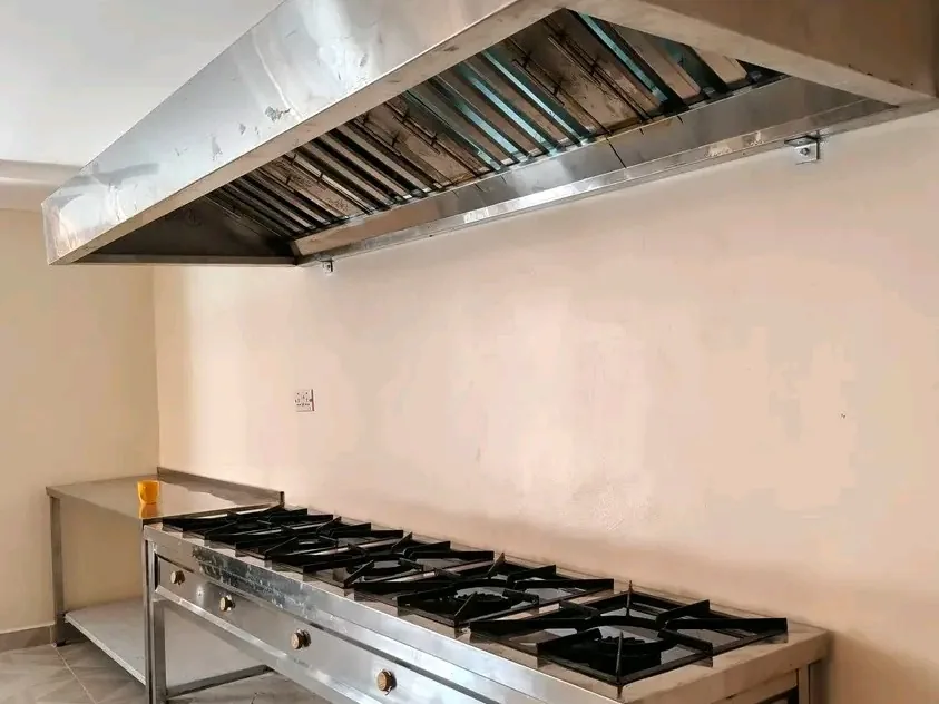 Commercial kitchen gas burner range installed beneath a stainless steel extraction hood