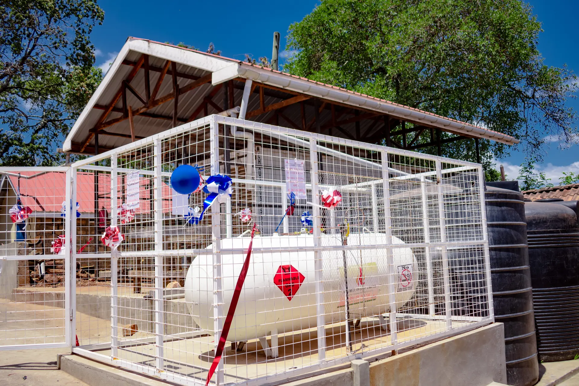Bulk LPG storage tank inside a white steel safety enclosure, decorated for a commissioning ceremony